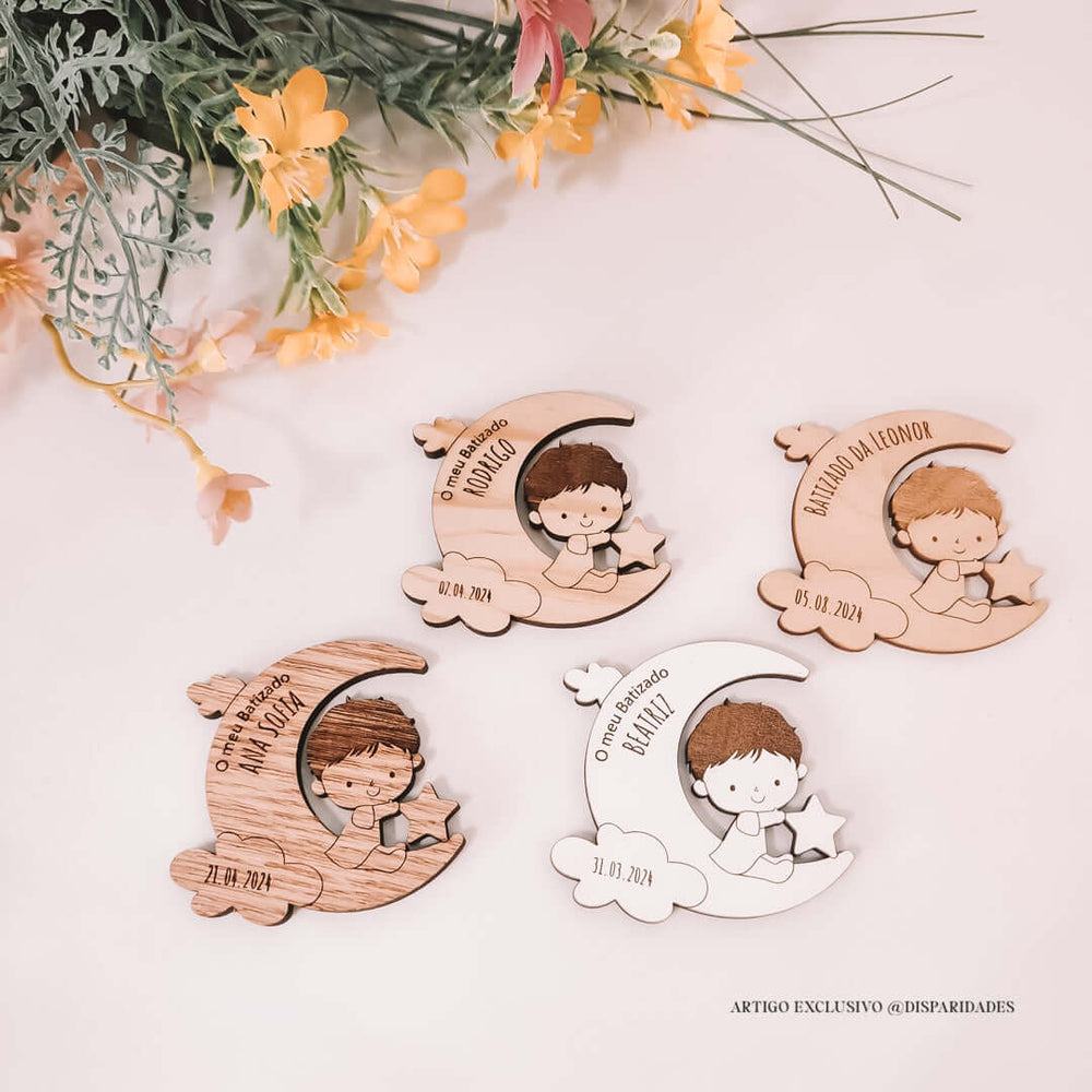 Lembranças de batizado em madeira com formatos de lua e estrela, personalizadas com nomes e datas, ao lado de flores artificiais. Estilo rústico e infantil.