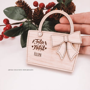 Mealheiro porta-cartões em madeira, com laço e gravação 'Feliz Natal Filipa', ao fundo decorado com pinhas e bagas. Mealheiro porta-cartões em madeira, com laço e gravação 'Feliz Natal Filipa', ao fundo decorado com pinhas e bagas.