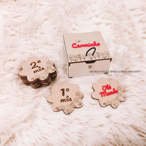 Placas de madeira em forma de flor, numeradas "1º mês" e "2º mês", ao lado de uma com "Olá Mundo" em rosa. Caixa decorada com nome "Carminho" ao fundo. Perfeitas para registrar milestones do bebé. Placas de madeira em forma de flor, numeradas "1º mês" e "2º mês", ao lado de uma com "Olá Mundo" em rosa. Caixa decorada com nome "Carminho" ao fundo. Perfeitas para registrar milestones do bebé.