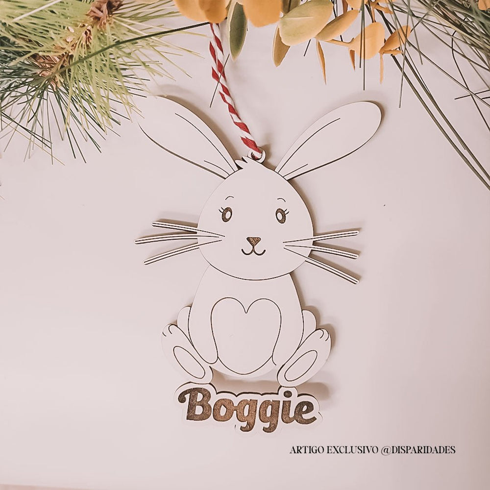 Pendente coelho com design minimalista em madeira, detalhes faciais simples e coração no peito. Pendura-se com fio vermelho e branco. Nome “Boggie” na base.