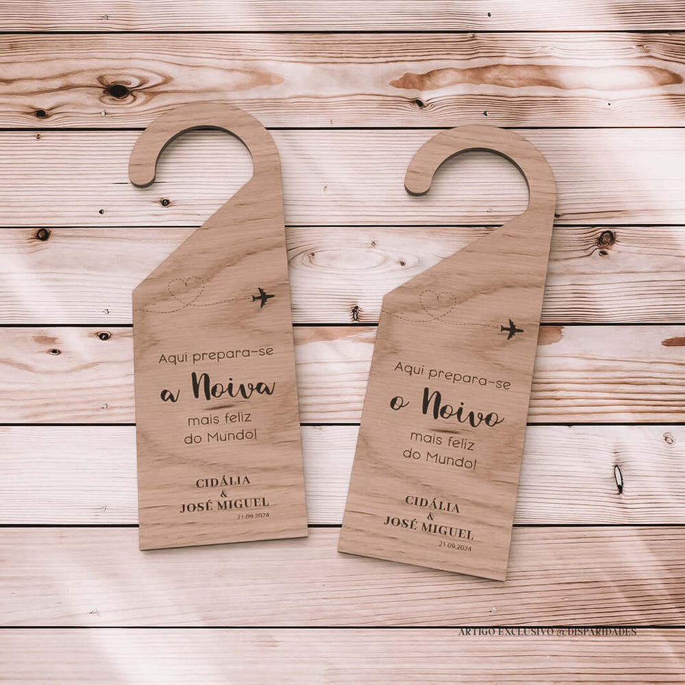 Placas de cabide em madeira com veios naturais, destinadas à noiva e ao noivo. A esquerda anuncia "Aqui prepara-se a Noiva mais feliz do Mundo!" e a direita "Aqui prepara-se o Noivo mais feliz do Mundo!", referindo-se ao casamento de Cidália e José Miguel em 21.09.2024