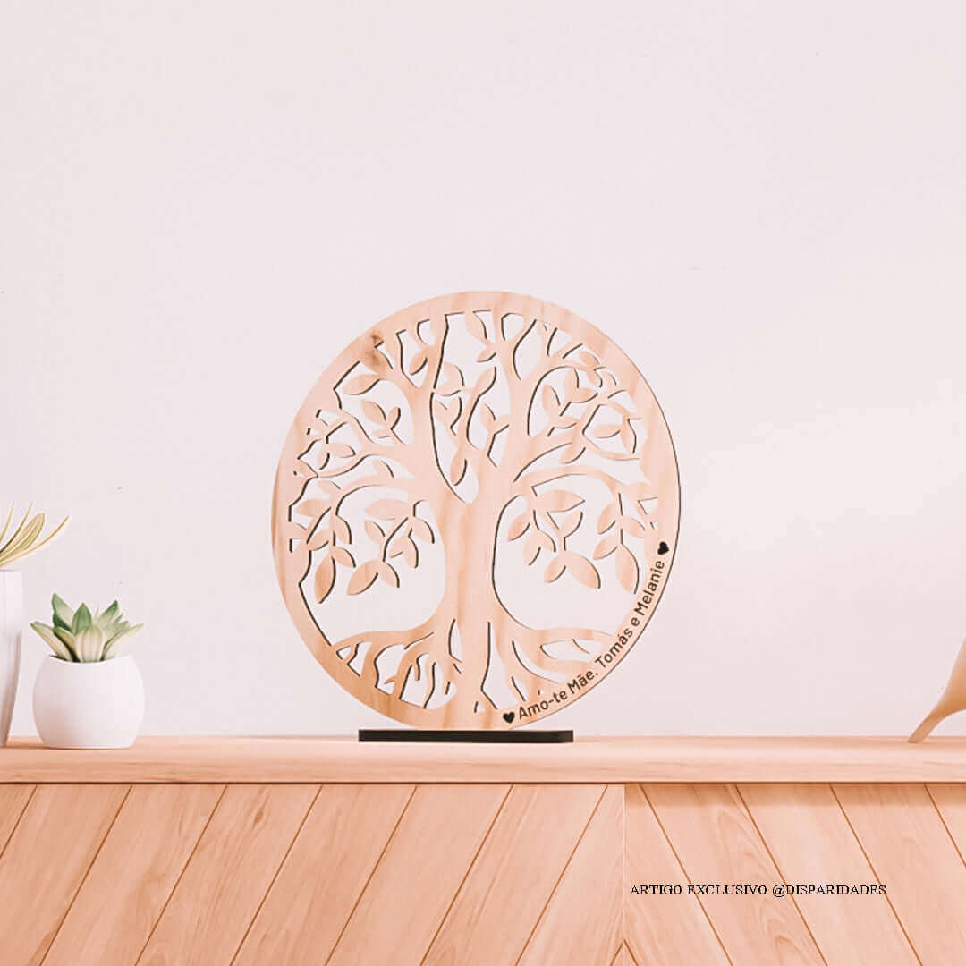 Decoração de interiores com uma peça de madeira clara em forma de árvore da vida sobre uma prateleira de madeira, personalizada com 'Amo-te Mãe - Tomás e Melanie' em um ambiente doméstico