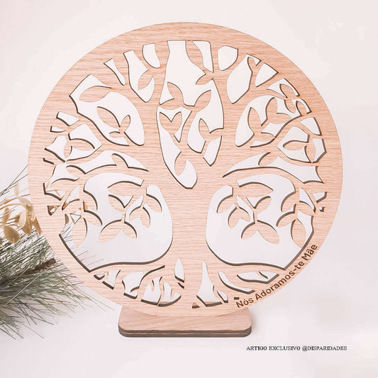 Ornamento de madeira em forma de árvore com corte a laser, com texto 'Nós Adoramos-te Mãe', apoiado em uma base de madeira escura, com decoração festiva ao fundo