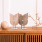 Duas asas de anjo em madeira sobre pedestal, ao lado de uma esfera de madeira e galho seco.
