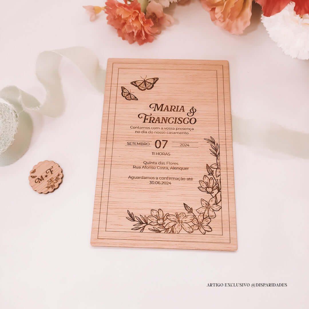 Convite de casamento rústico em madeira com nomes "Maria & Francisco", detalhes florais gravados e data. Pequeno botão em madeira ao lado.