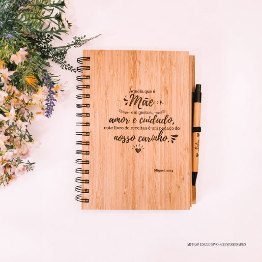 Caderno rústico com dedicatória para mãe e caneta, junto a flores silvestres, em fundo claro.
