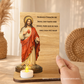 Placa de madeira com imagem do Sagrado Coração de Jesus e vela acesa, com oração religiosa gravada em português.
