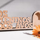 Peça decorativa em madeira com a inscrição "OS NETOS DOS AVÓS" ao lado de um coração e uma flor laranja.