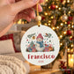 Mão a segurar uma bola de Natal personalizada com boneco de neve, nome Francisco e ano 2026, com árvore iluminada ao fundo.
