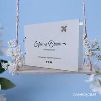 Capa para livro de honra em branco personalizado como o nome dos noivos, data e mensagem, tema viagens, colocada sobre um baloiço  com flores brancas e um fundo azul