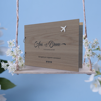Capa para livro de honra em carvalho personalizado como o nome dos noivos, data e mensagem, tema viagens, colocada sobre um baloiço  com flores brancas e um fundo azul