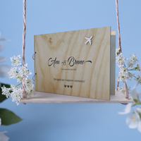 Capa para livro de honra em pinho personalizado como o nome dos noivos, data e mensagem, tema viagens, colocada sobre um baloiço com flores brancas e um fundo azul
