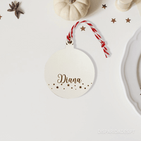 Bola de Natal branca com um fio para pendurar branco e vermelho em cima de uma mesa com pequenas estrela