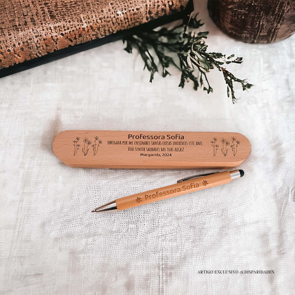Estojo rústico de madeira com dedicatória para "Professora Sofia", acompanhado de uma caneta personalizada. Fundo decorativo com plantas e tecido claro.