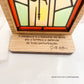 Oratório rústico com vitral iluminado de Santo António a segurar o Menino Jesus, com frase sobre paciência gravada na base em madeira.