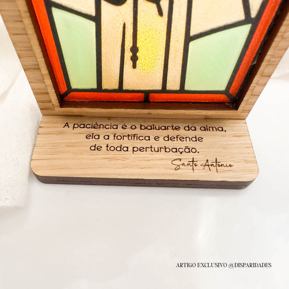 Oratório rústico com vitral iluminado de Santo António a segurar o Menino Jesus, com frase sobre paciência gravada na base em madeira.