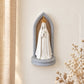 Oratório de Nossa Senhora de Fátima fixo na parede, com figura branca, coroa dourada, fundo em madeira e arco cinzento.