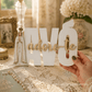 Mão segura placa branca “AVÓ adoro-te” com Nossa Senhora de Fátima sobre mesa com renda e terço.