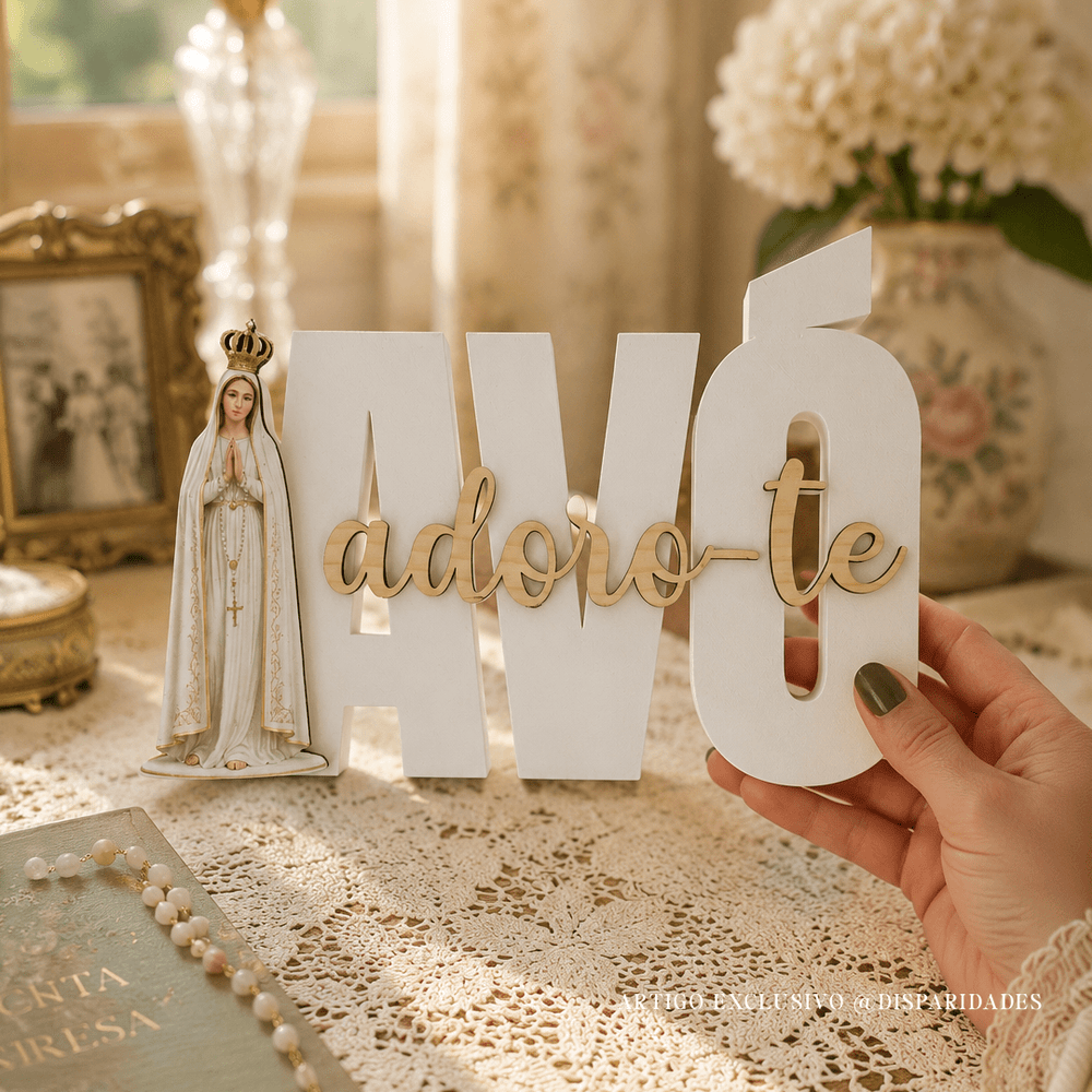 Mão segura placa branca “AVÓ adoro-te” com Nossa Senhora de Fátima sobre mesa com renda e terço.