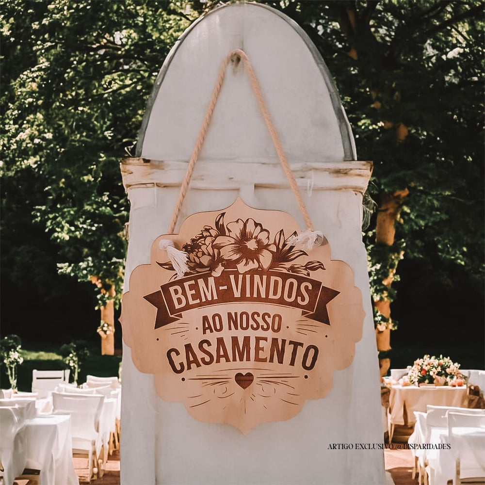 Placa rústica de madeira pendurada com a mensagem "Bem-vindos ao nosso casamento", decorada com flores. Emoldurada por flores naturais em ambiente romântico e acolhedor.