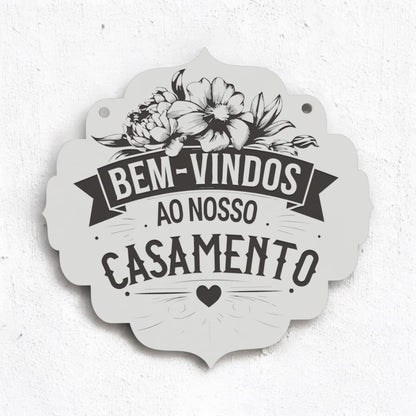 Placa rústica em madeira clara com flores desenhadas e a frase "Bem-vindos ao nosso casamento". Fundo branco, realçando o design simples e acolhedor.
